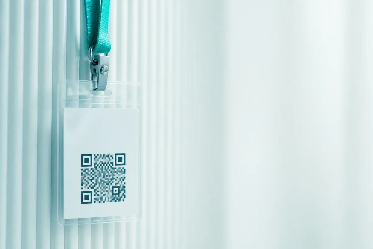 A blank event badge in a clear holder hanging from a lanyard against a venue wall.